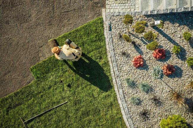 Landscaping and Gardening. Aerial View of Gardener Installing Brand New Grass in Newly Developed Residential Garden. Industrial Theme.