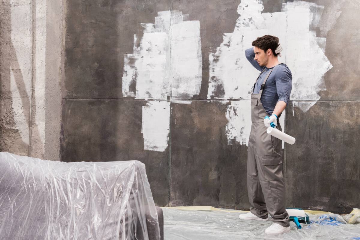 side view of confused young man with paint roller renovating home
