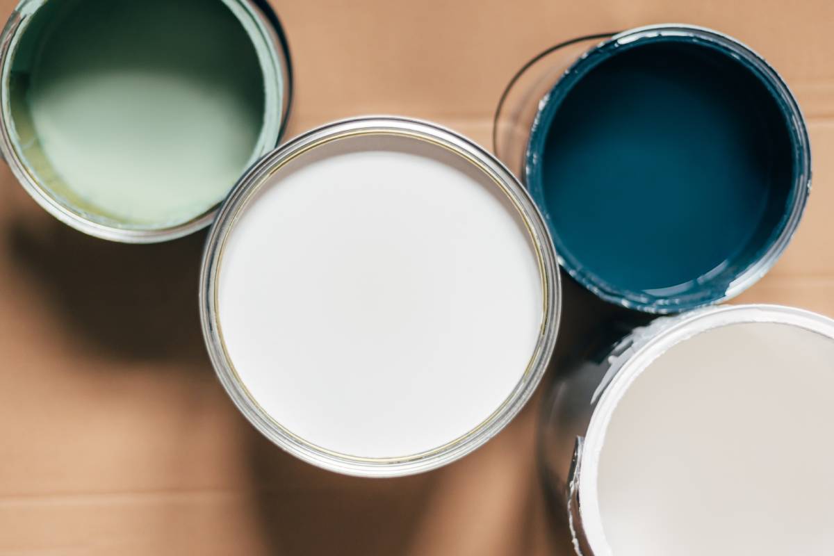 Paint cans during house renovation, process of choosing paint for the walls, different colors of white, green and blue on wooden floor
